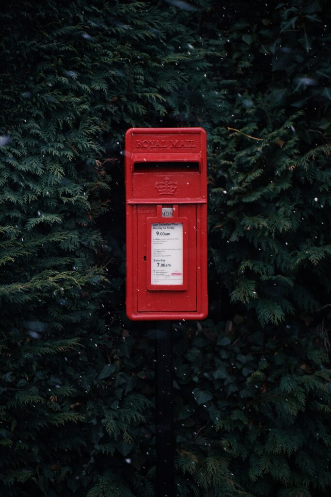 A small red postbox against a background of dark green foliage